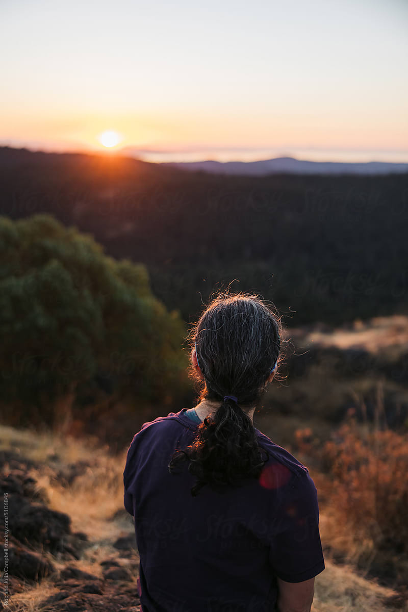 Woman sitting on hilltop watching sunrise.