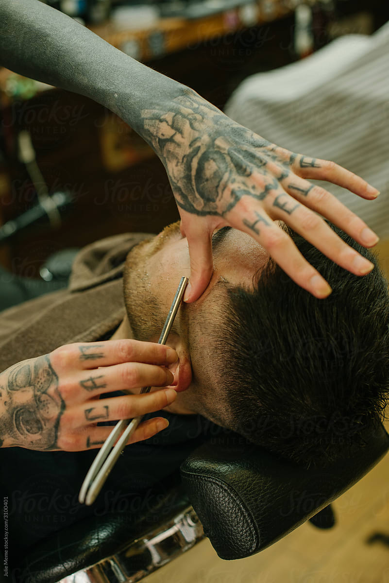 Closeup photo of a barber’s hands Shaving a dark hair guy with a razor