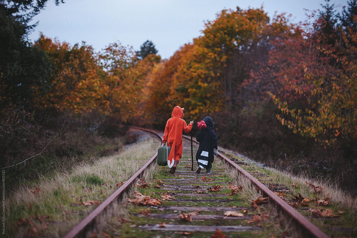 Kids dressed up like fox and raccoon walking on train tracks