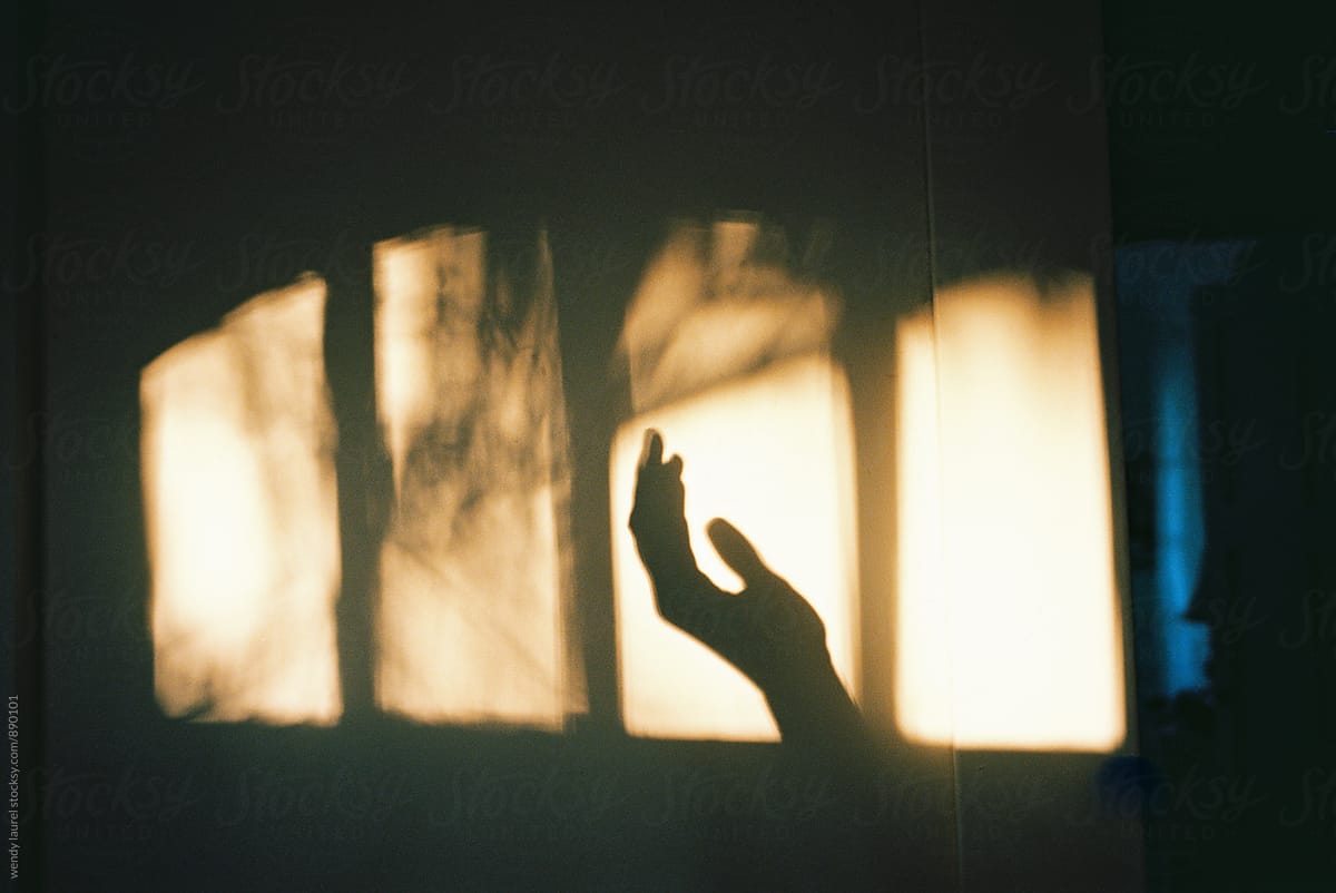 shadow of hand in window on wall with golden light