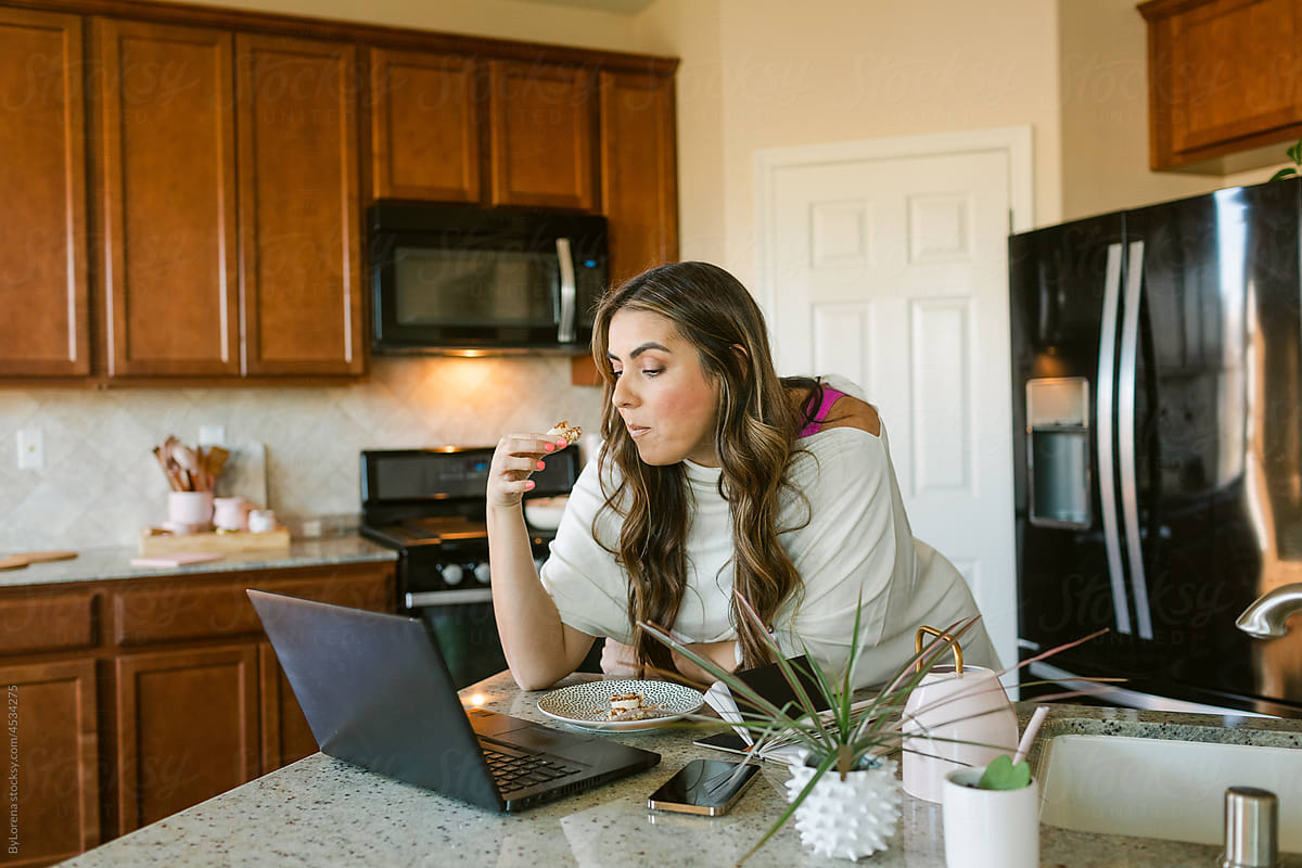 Woman having breakfast while looking at laptop in kitchenette