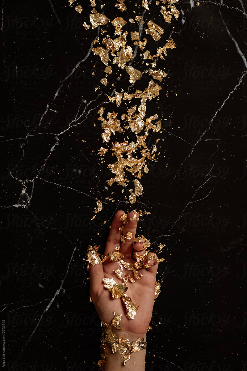 woman hand and gold leaf petals on black marble