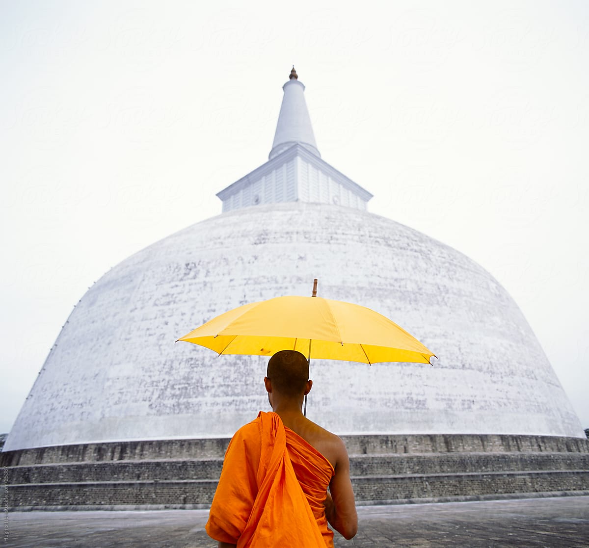 Buddhist monk holding umbrella standing in front of dagoba. Sri Lanka.