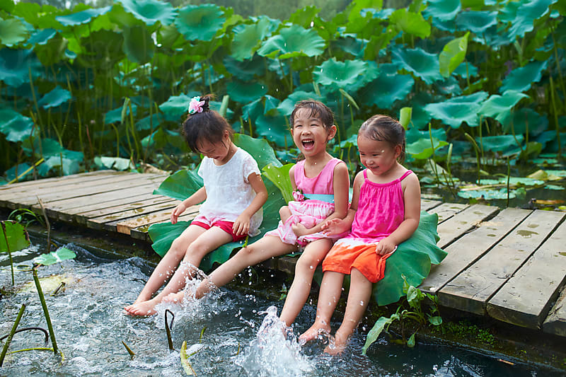 Three little girls sitting by the pond playing water