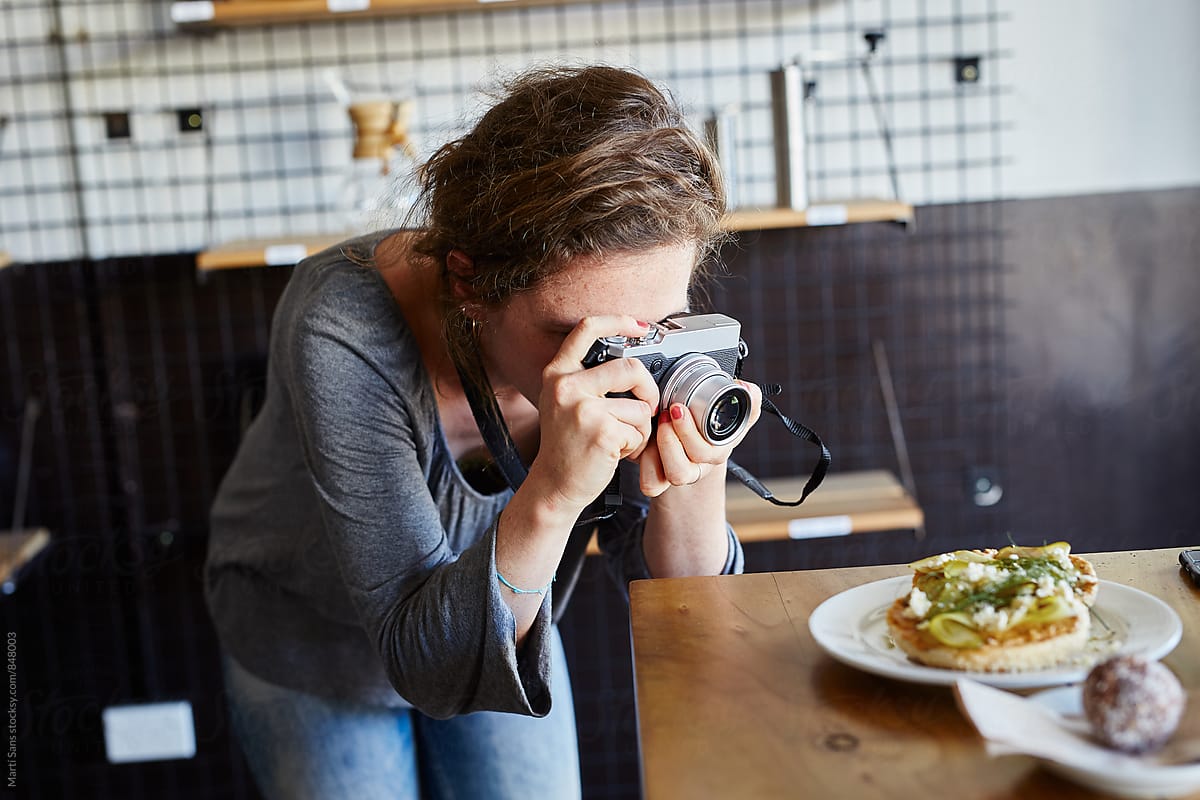 Woman taking photo of food in café with analog camera