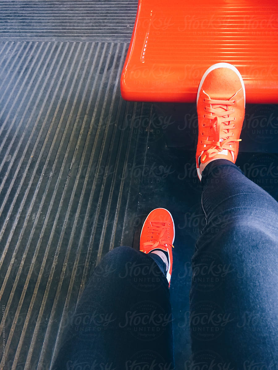 Pov of person wearing neon orange sneakers matching to plastic seat