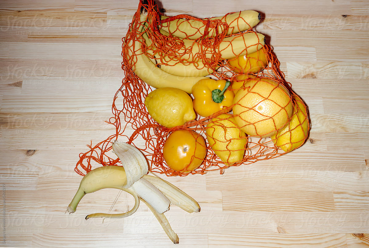 Bitten banana near mesh bag with yellow vegetables and fruits