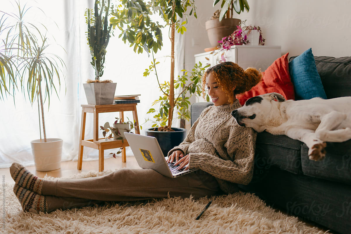 Woman working on laptop in home living room with dog