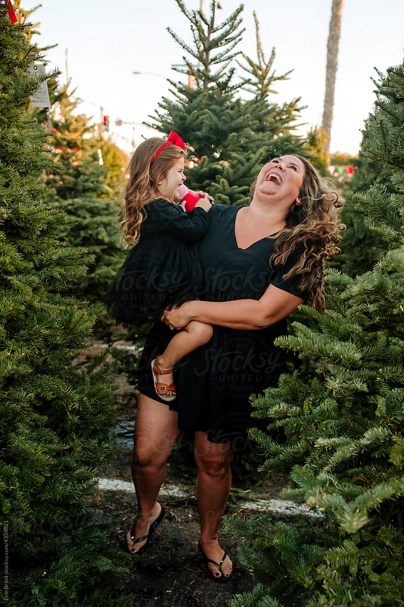 Joyful Mother holds daughter in front of pine trees