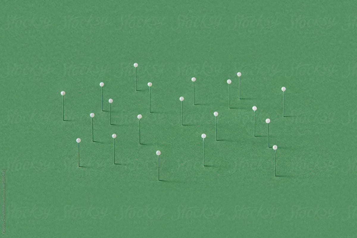Stationery straight pins stuck in green papercraft background