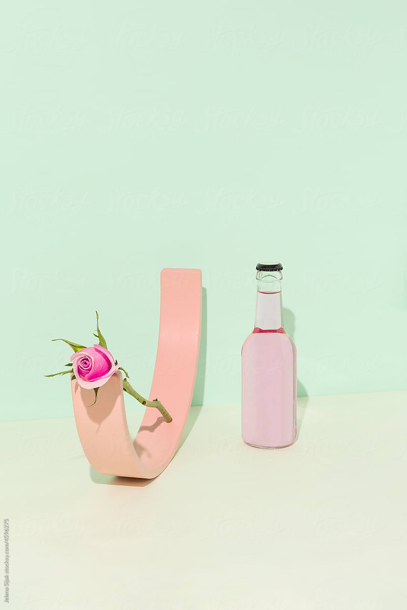 Pink tonic water for gin and one rose flower, green background a