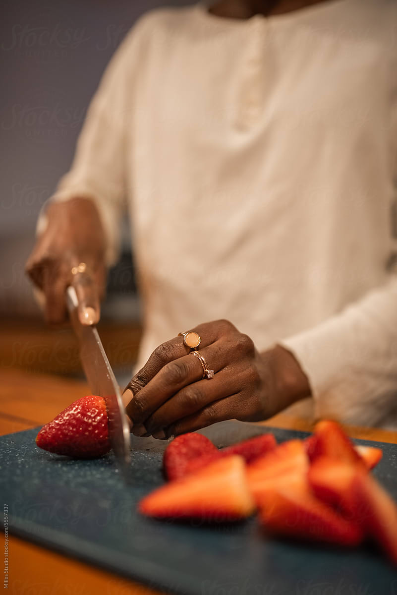 Crop black woman cutting strawberries in kitchen