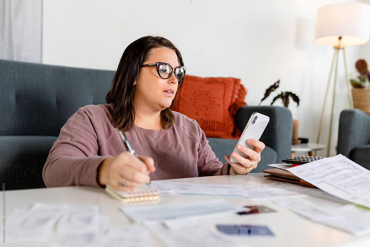 Woman Wearing Glasses Uses Phone to Calculate Annual Expenses and File Taxes