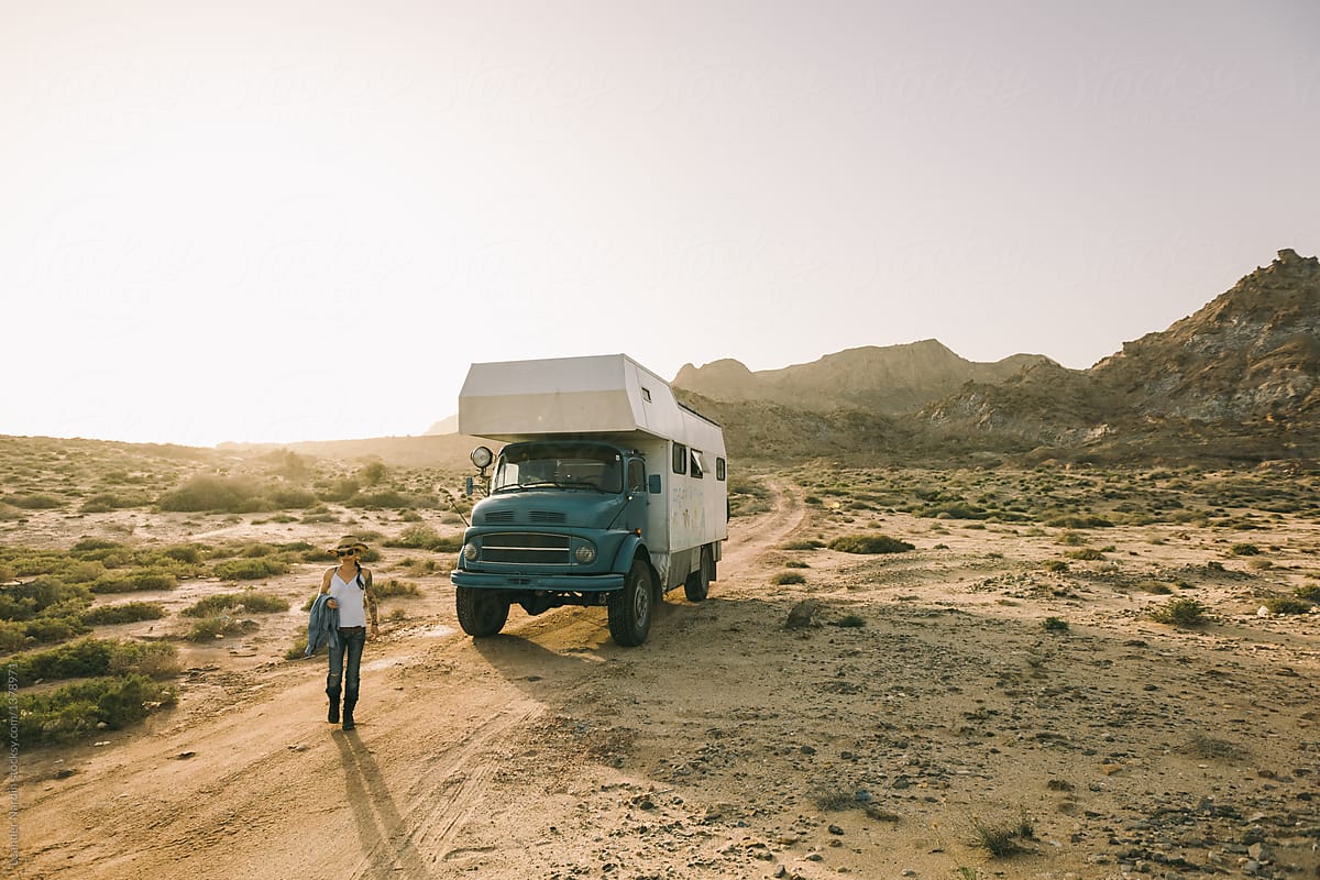 young woman walking in the desert beside a big camping truck