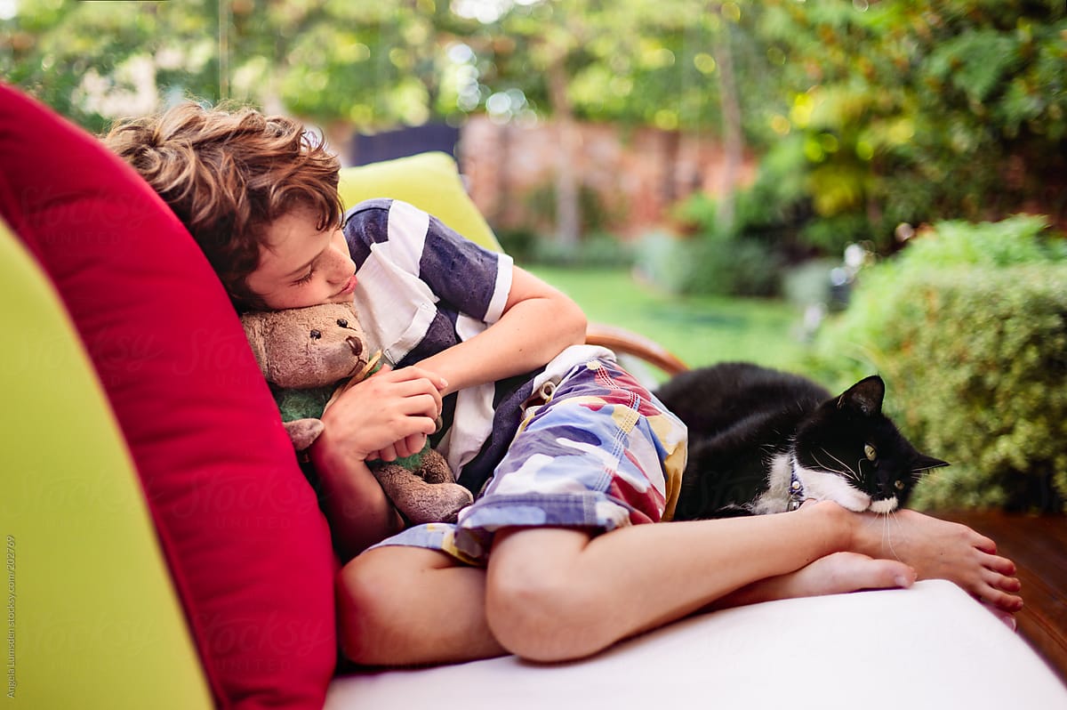 Child resting with cat and teddy bear in garden