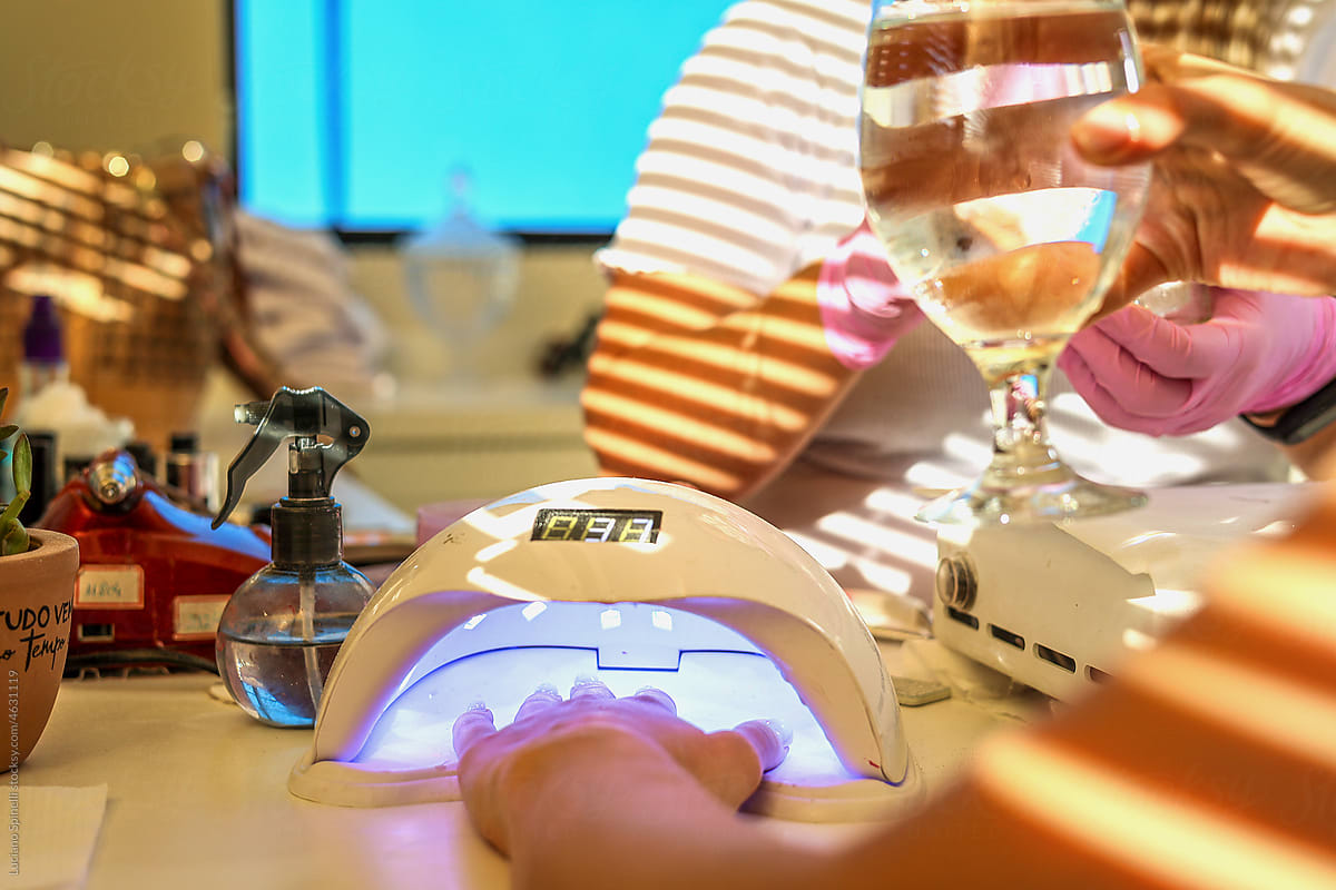 Woman drinks water while drying gel nail polish in a lamp in a salon