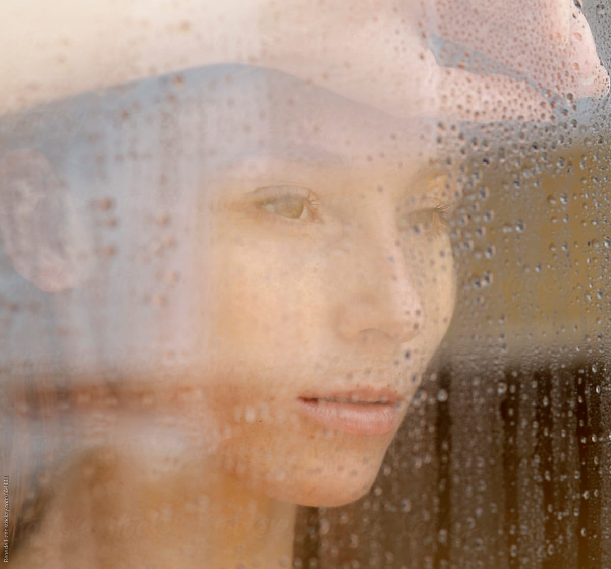 young woman  looking through window with raindrops