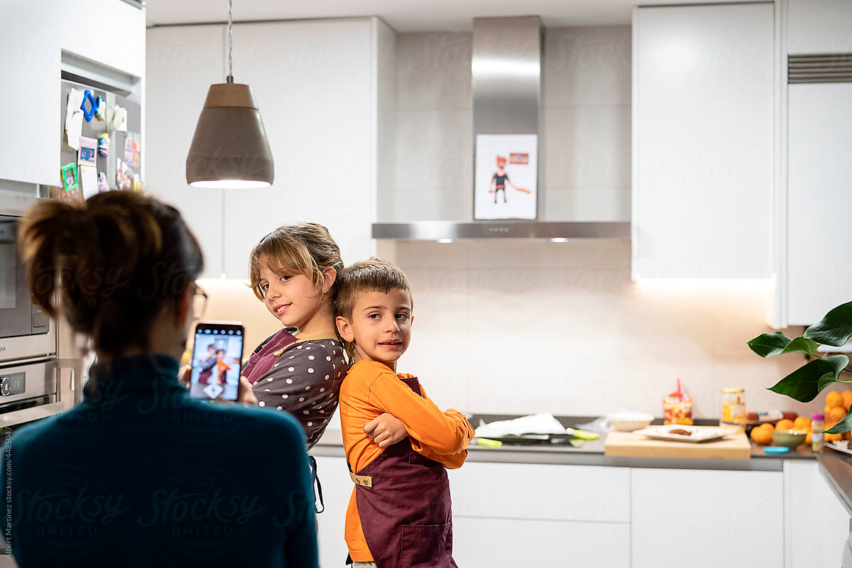 Mother taking photo of kids in home kitchen