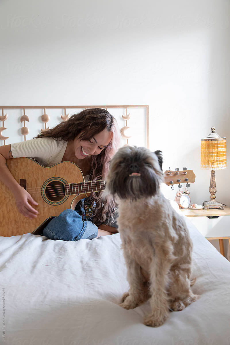 Beautiful woman at home writing music on her bed with her dog