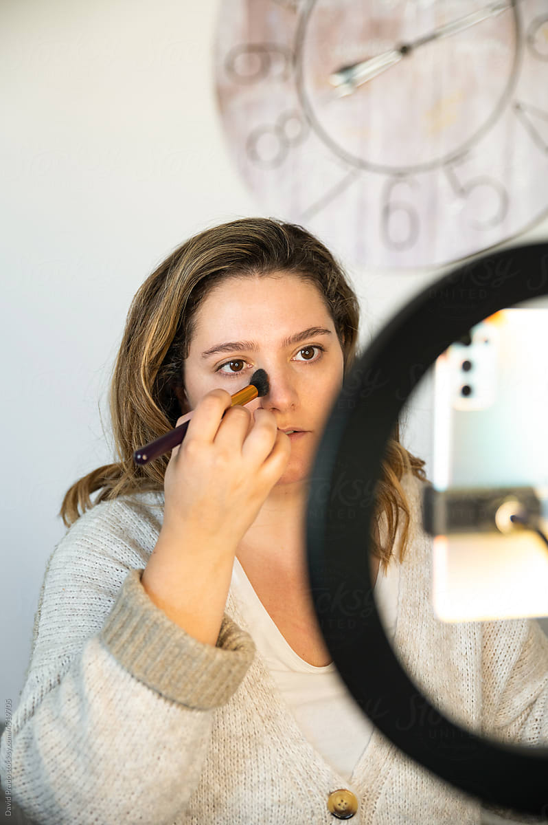 Woman applying makeup in front of smartphone and ring light