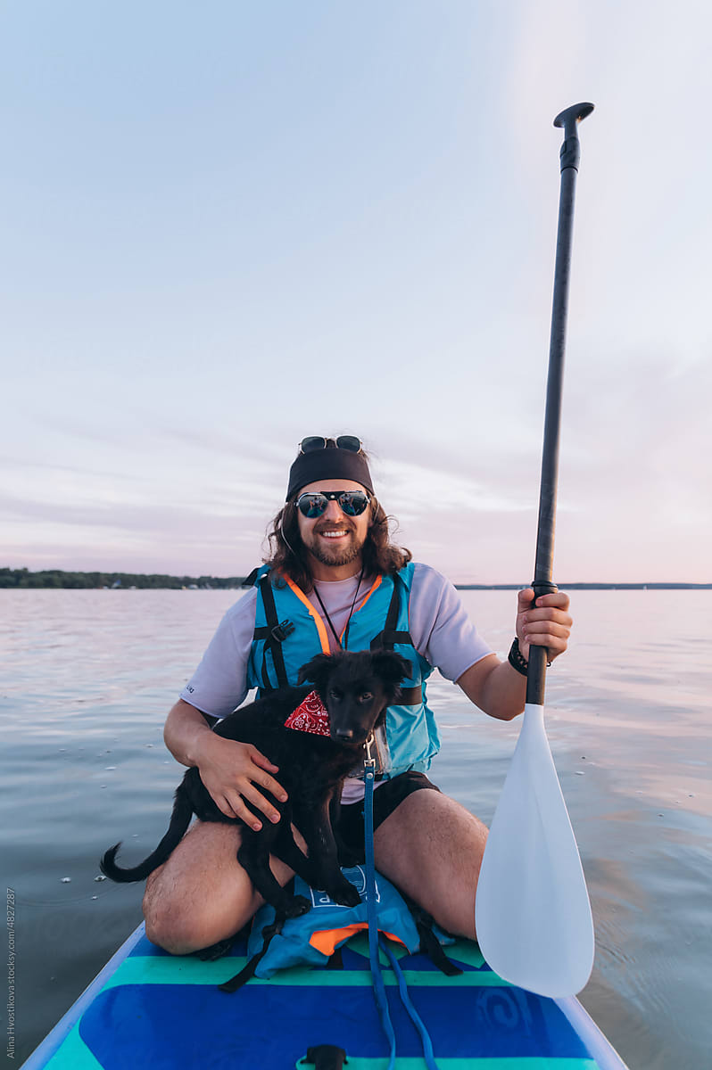 Happy man with dog floating on paddleboard in lake