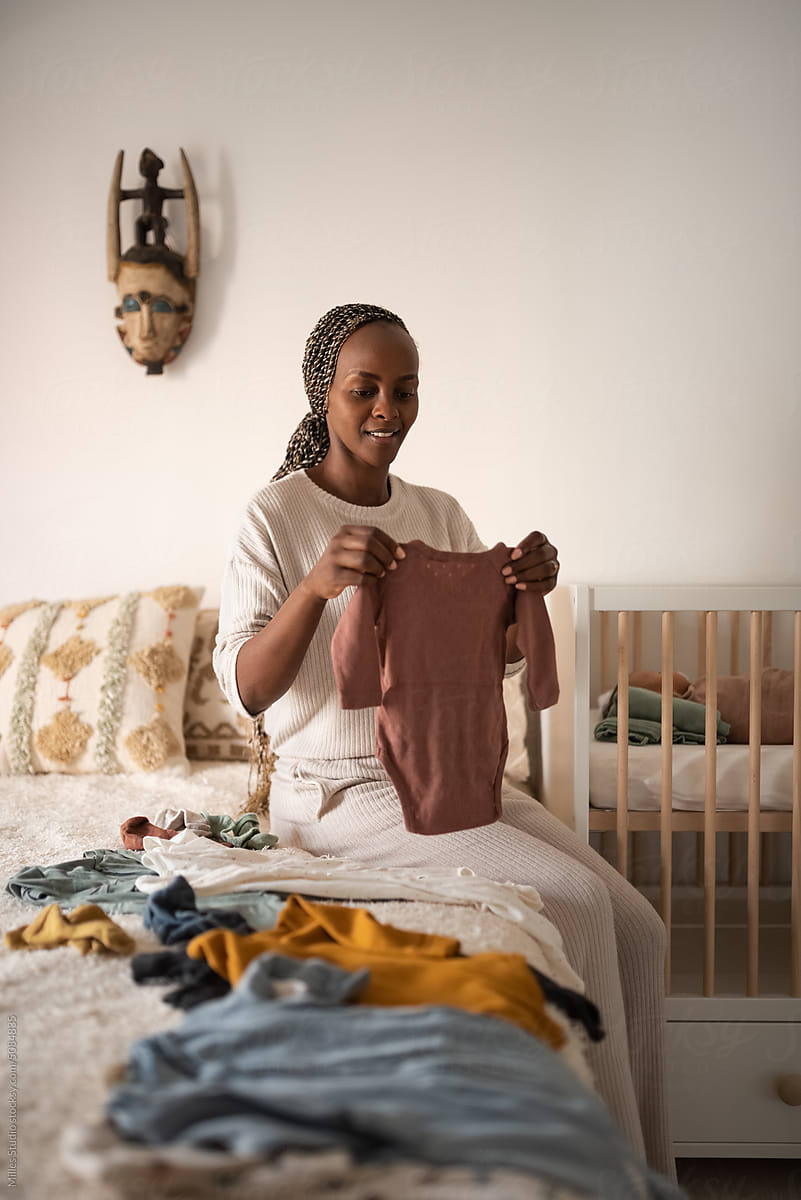 Black positive woman folding apparel of newborn