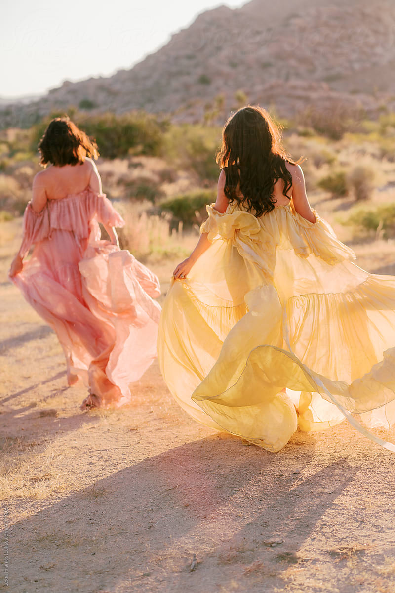 two women run in the desert wearing flowy bohemian maxi dresses
