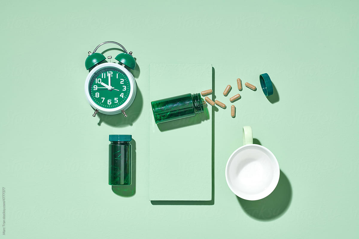 Green bottle with yellow pills, water of cup and alarm clock