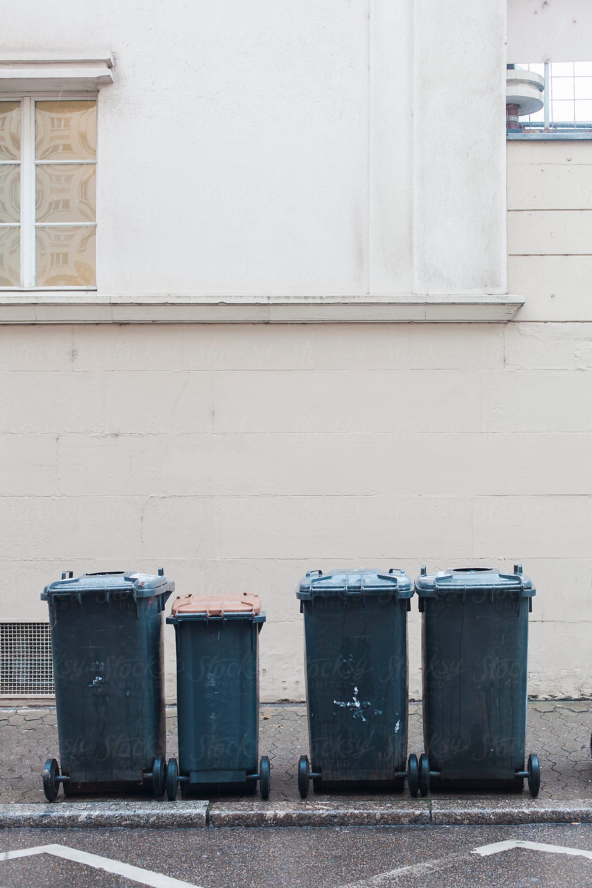 Four garbage bins against a wall in the street.