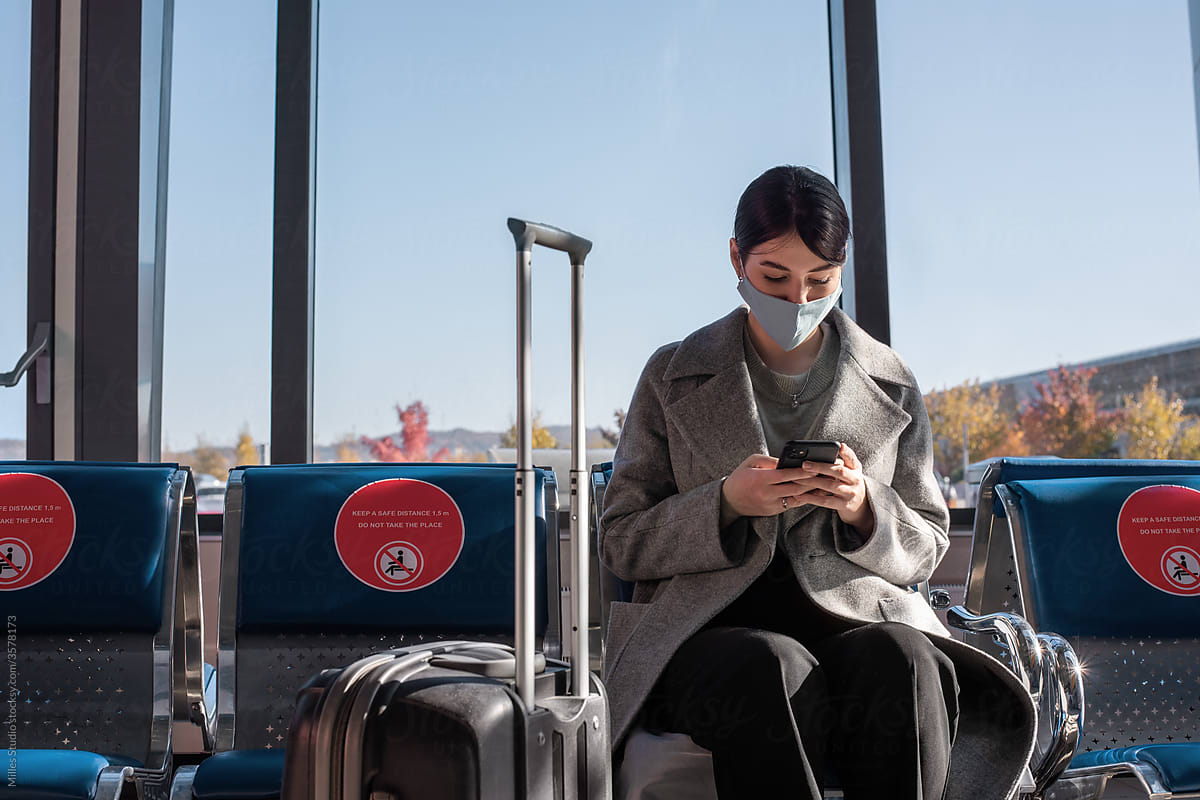 Woman in mask using smartphone in airport waiting room