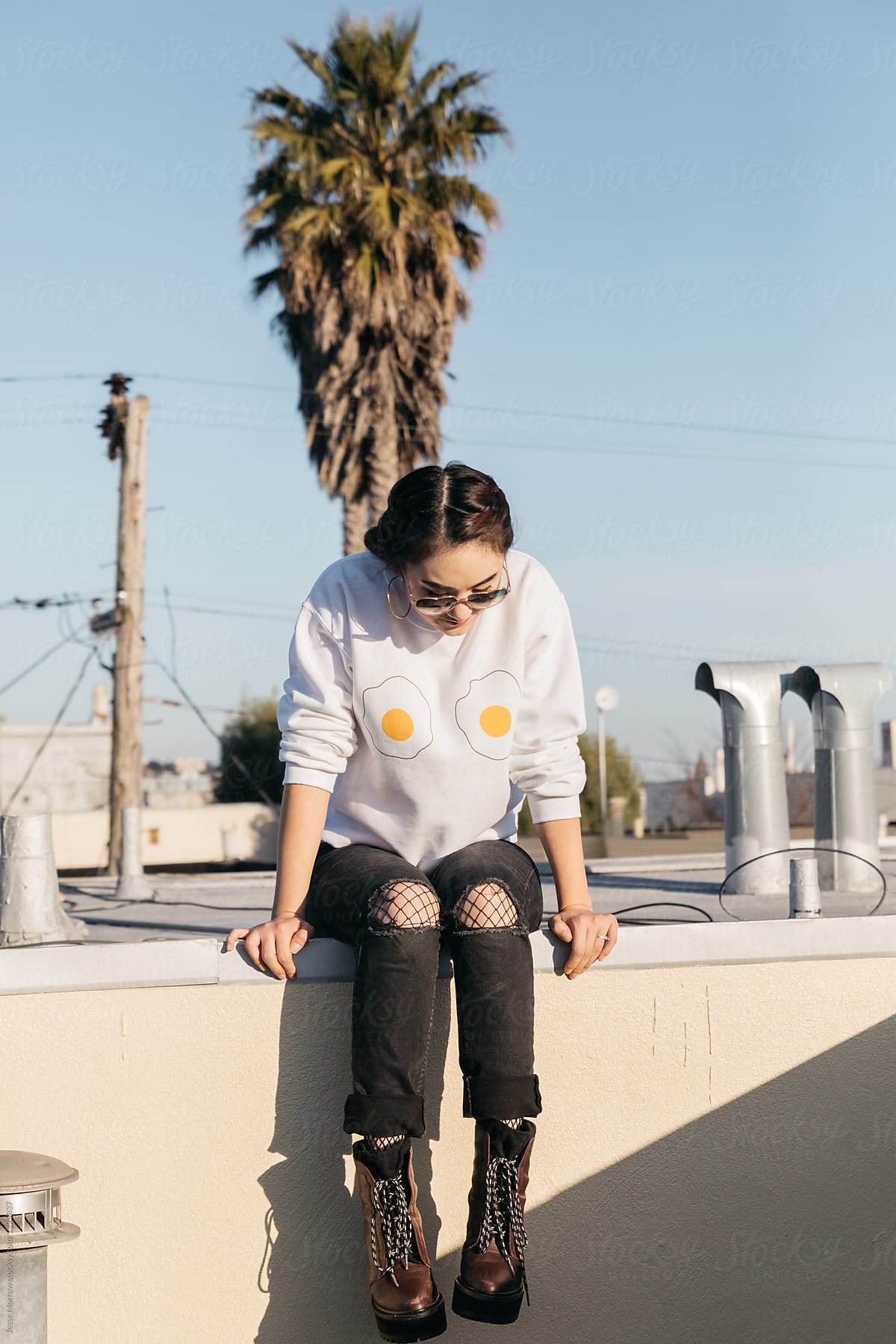 young woman wearing egg sweat shirt sitting on roof top in city