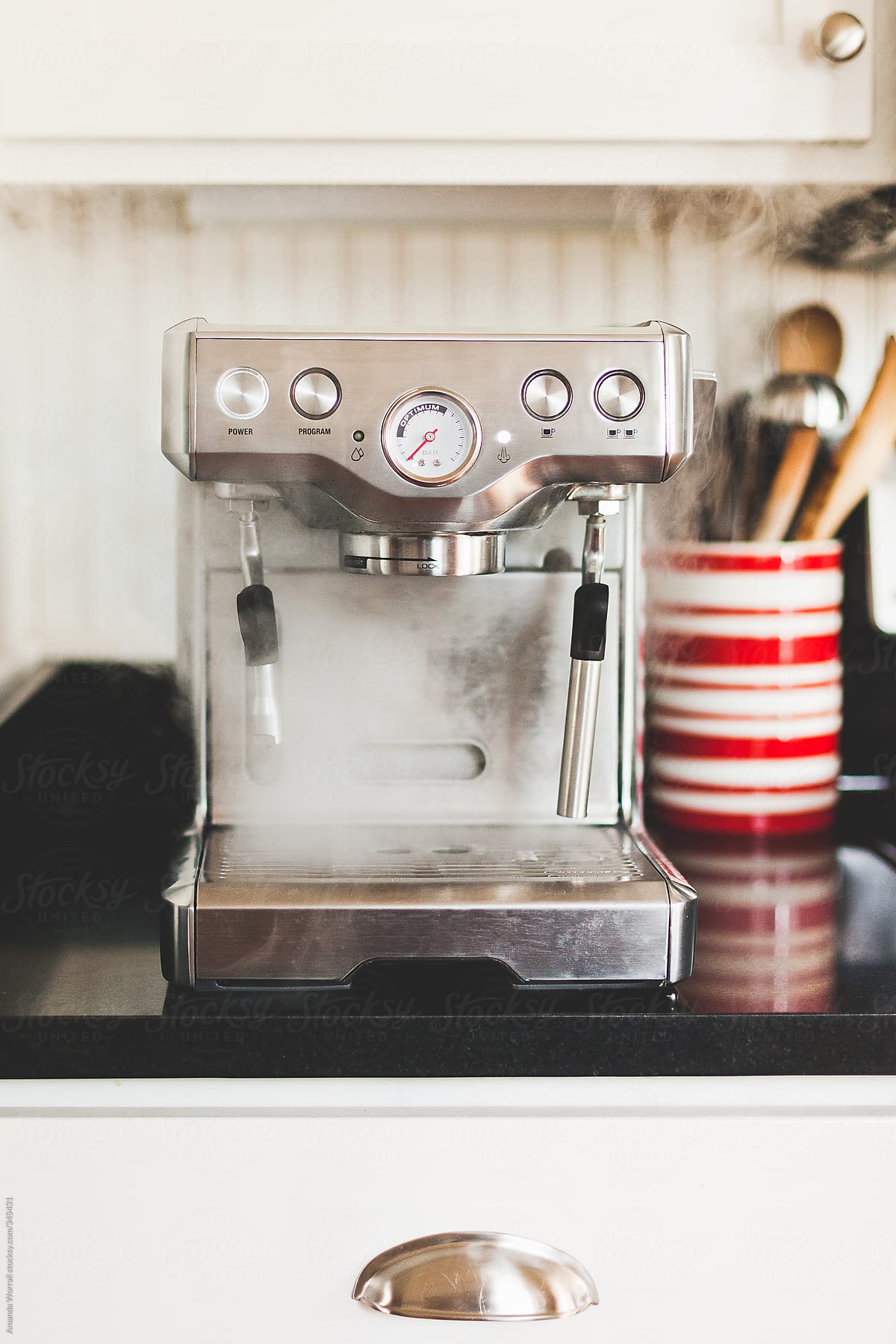 Steaming Espresso Machine sitting on counter with red and white striped utensil holder