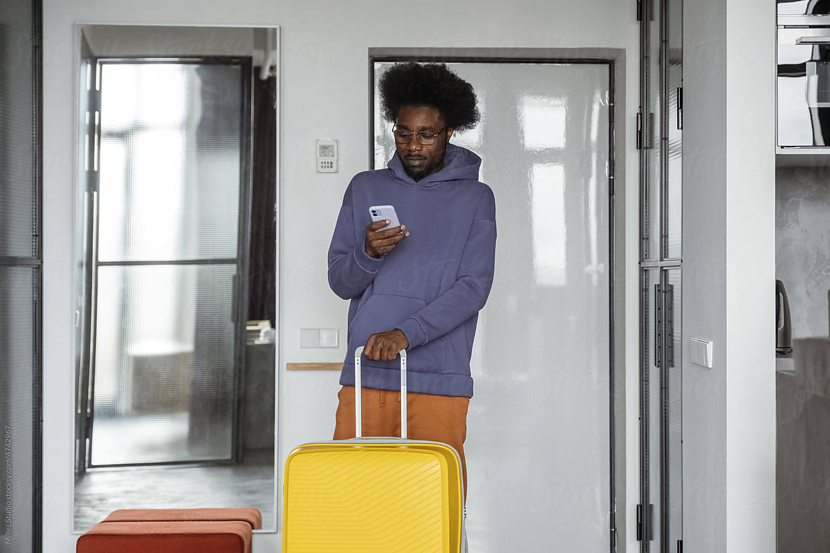 Black tourist with smartphone leaving apartment