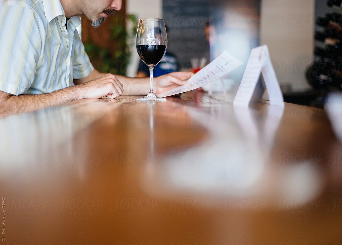 Man with glass of red wine looks at menu in a restaurant