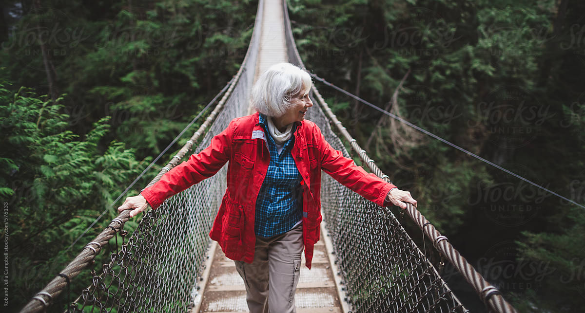 Attractive mature woman walking on suspension bridge through forest