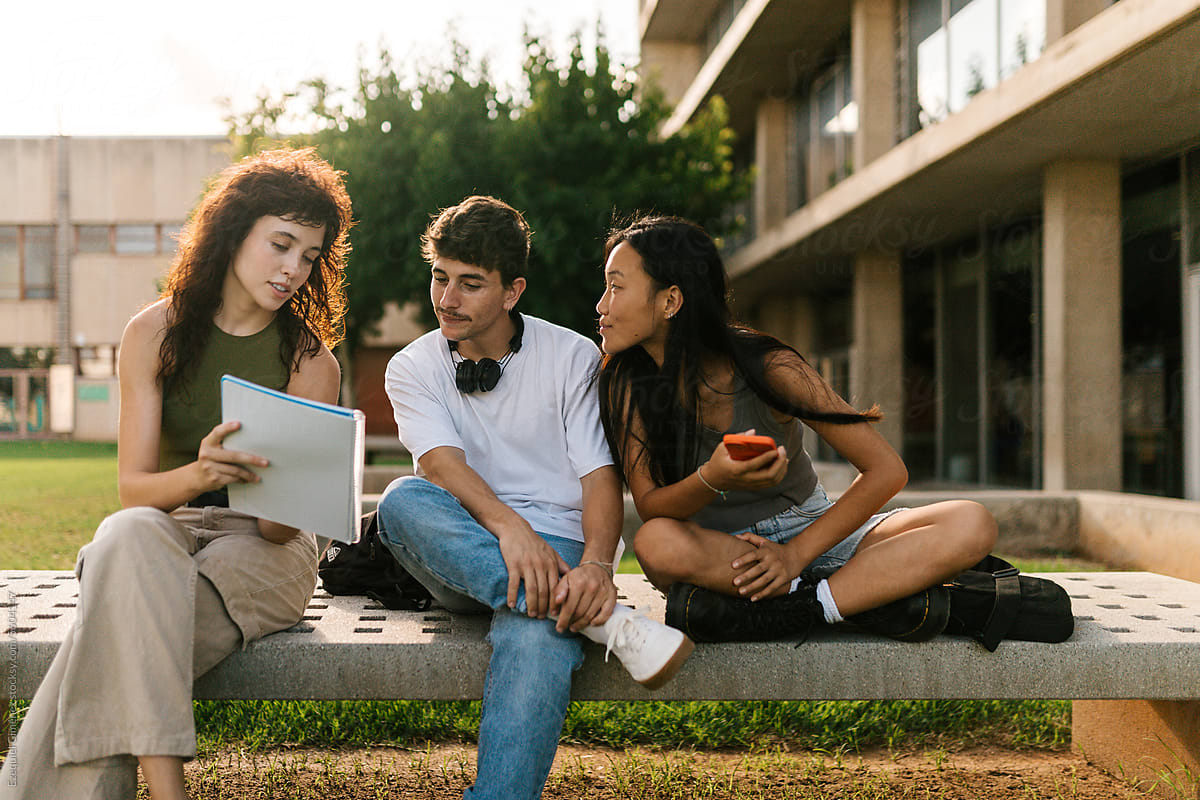 Diverse college classmates reading notes together on bench