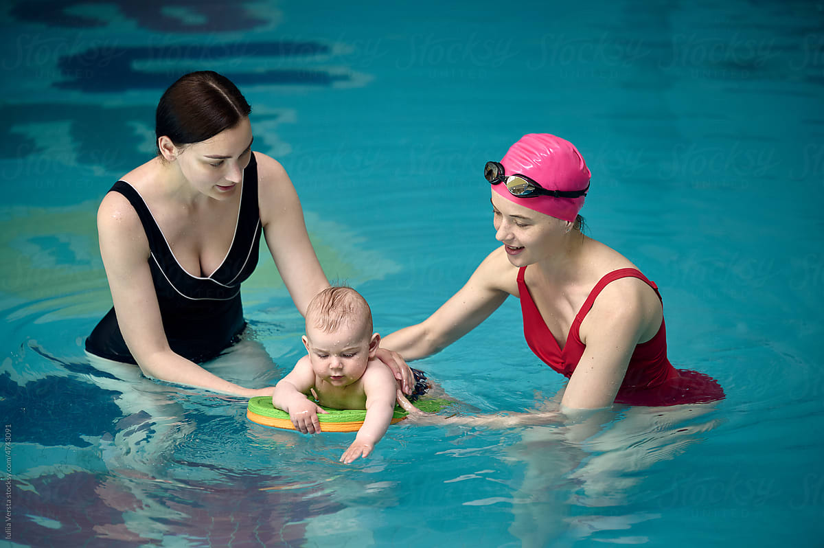 mother with a swimming coach teaching a baby to swim