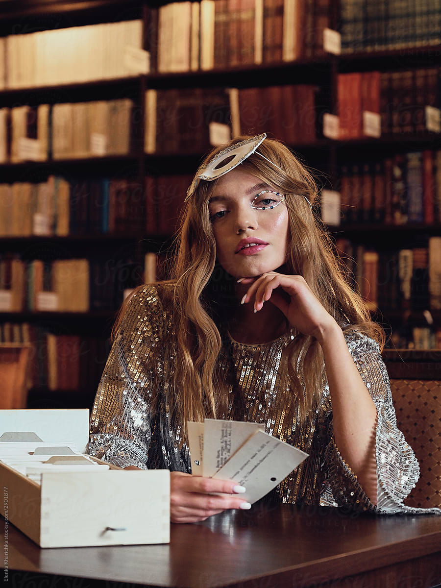 Young beautiful fashionable model sits in a library and plays cards