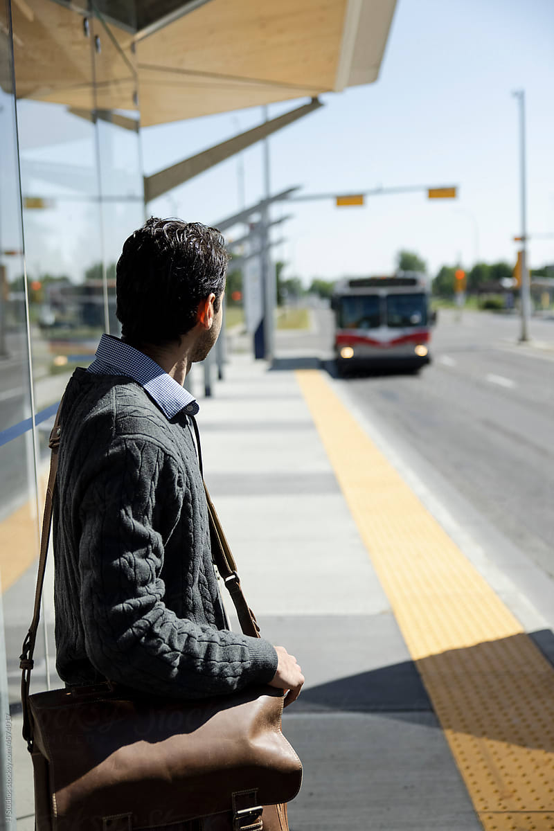 Man waiting for bus at sunny bus stop.