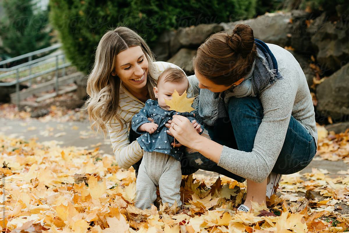 Two Lesbian Moms Looking At Fall Leaves With Infant Daughter Outside 7877