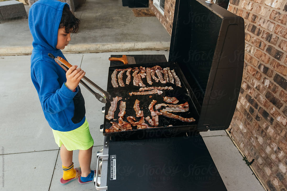 Boy cooking bacon on the grill.