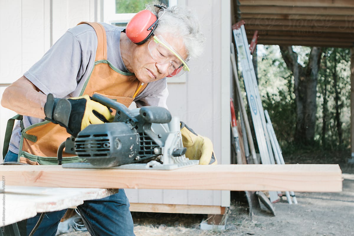 Elderly woman carpenter using circular hand saw to cut lumber