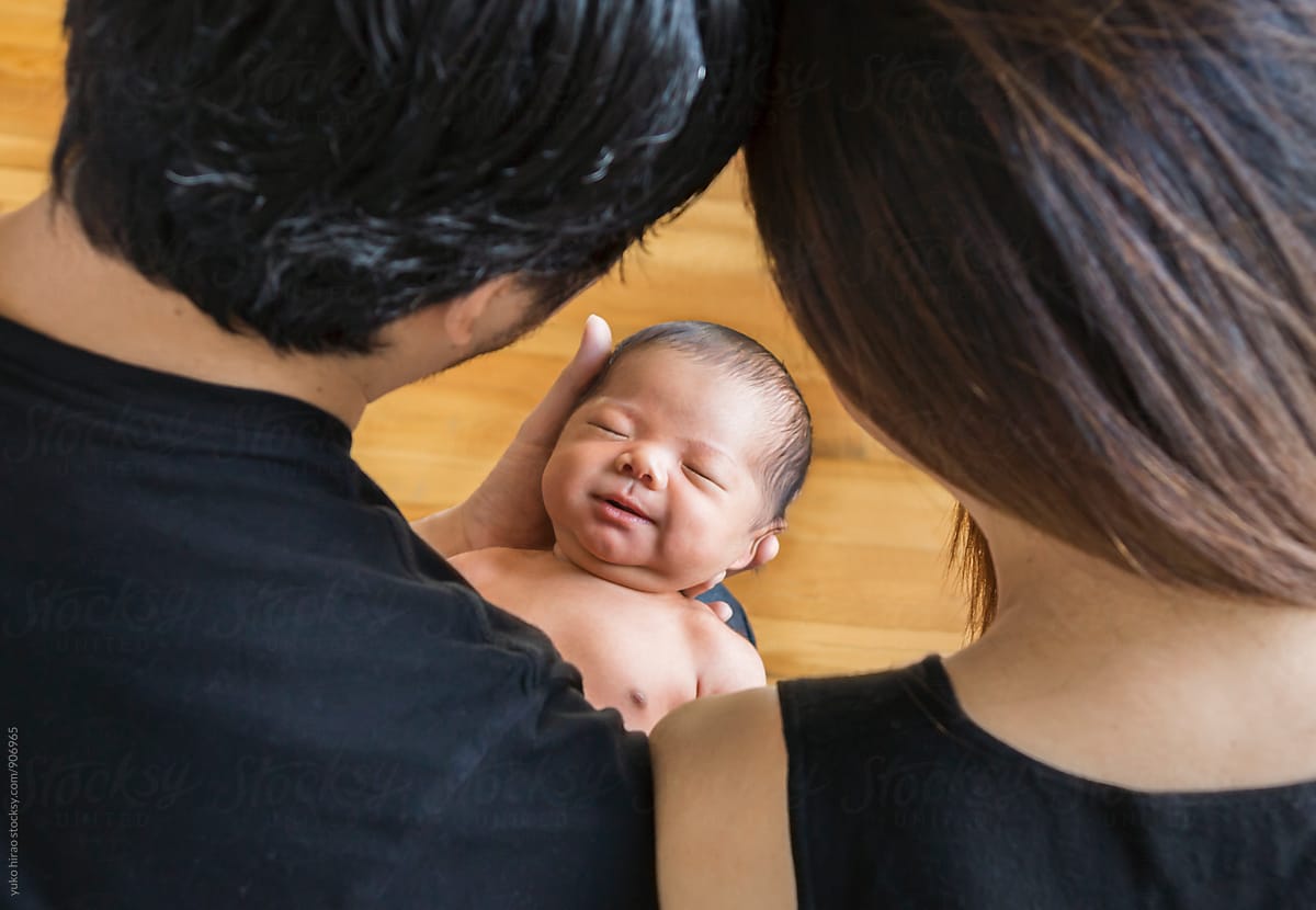 Smiley Asian newborn baby in parents\' arms