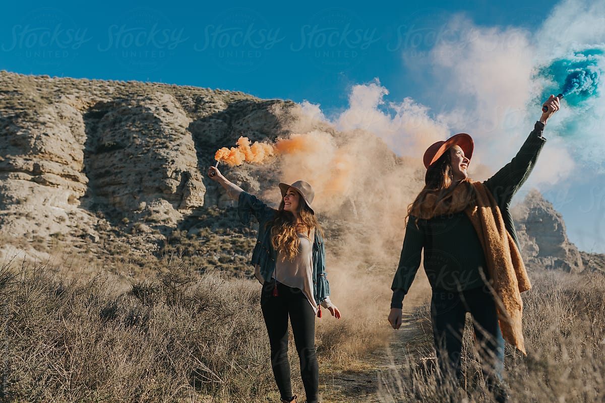 Cheerful teenagers playing with color smoke bombs in the countryside