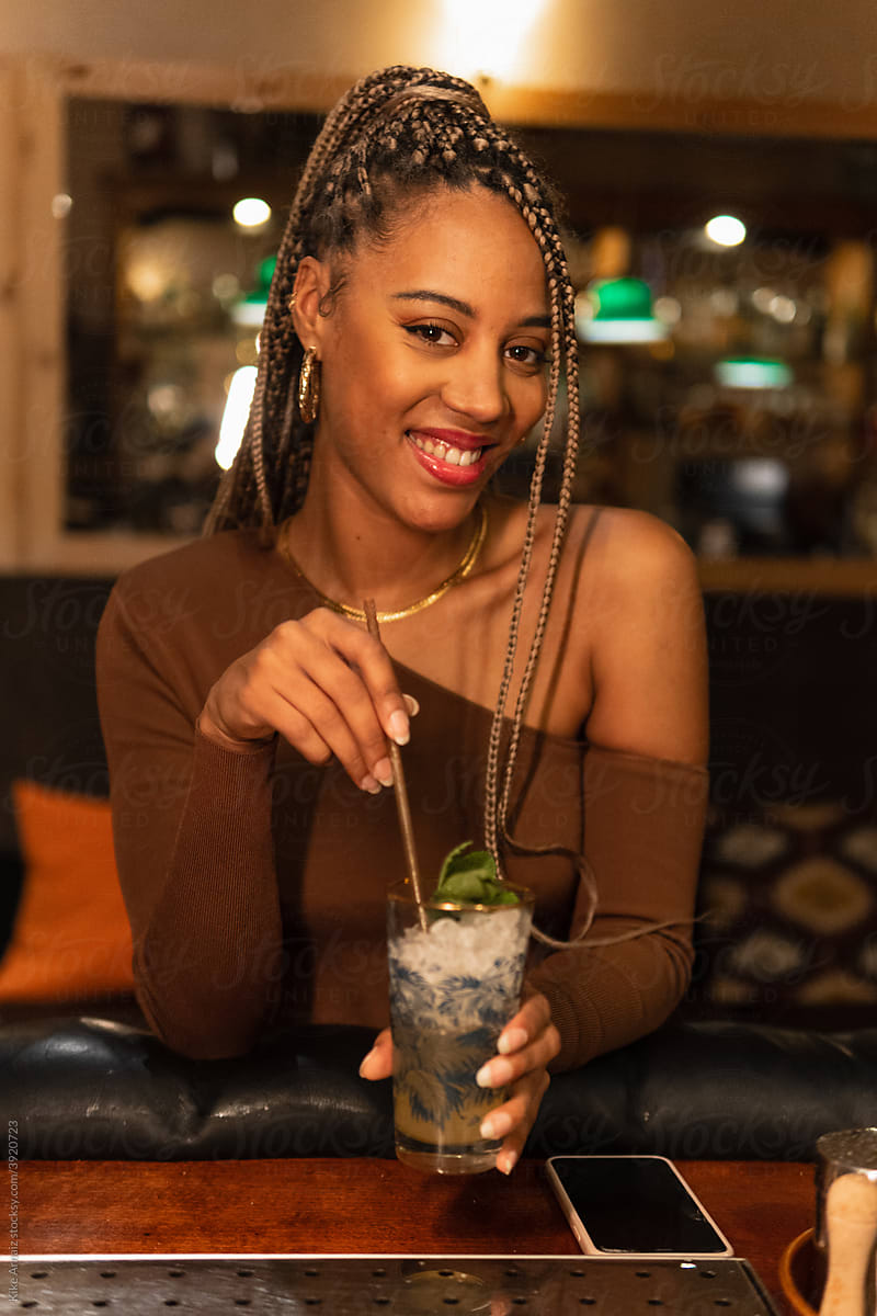 Happy black female with cocktail looking at camera