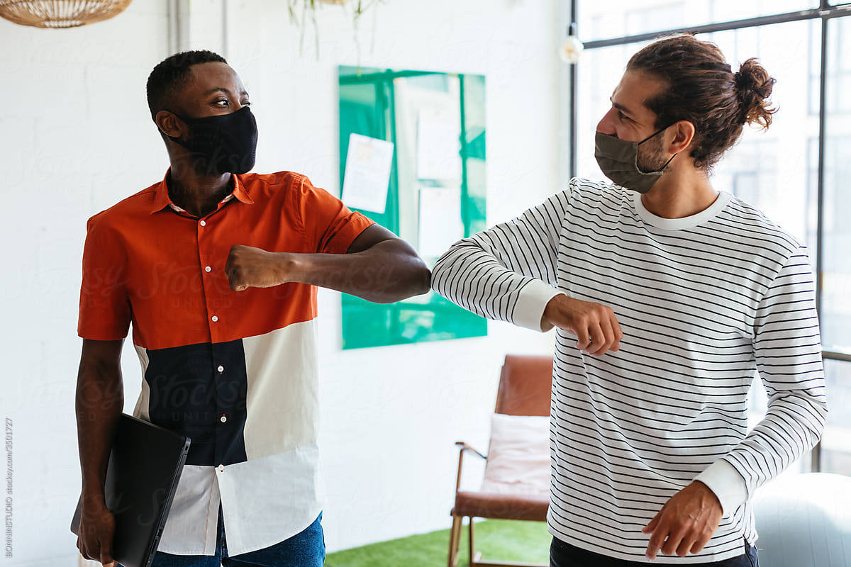 Multiethnic colleagues in masks bumping elbows in workspace