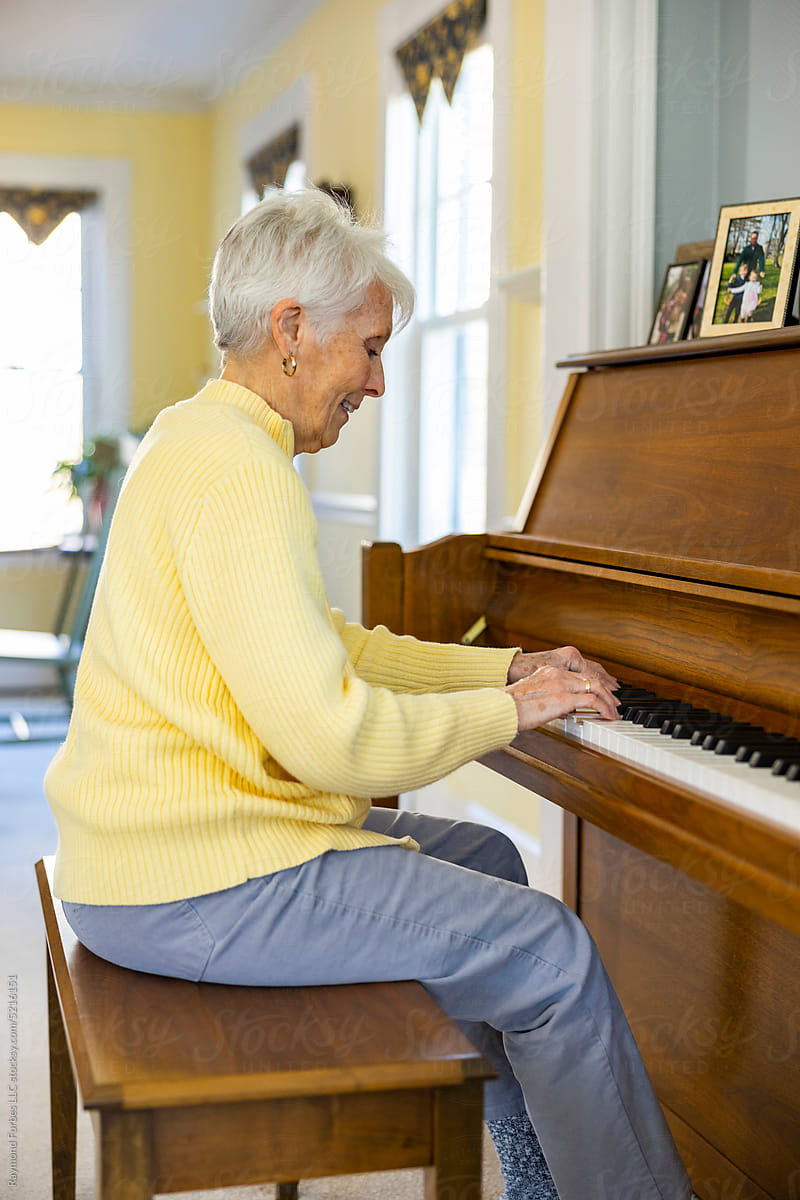 Happy Senior Citizen woman at Home playing piano keyboard in sweater