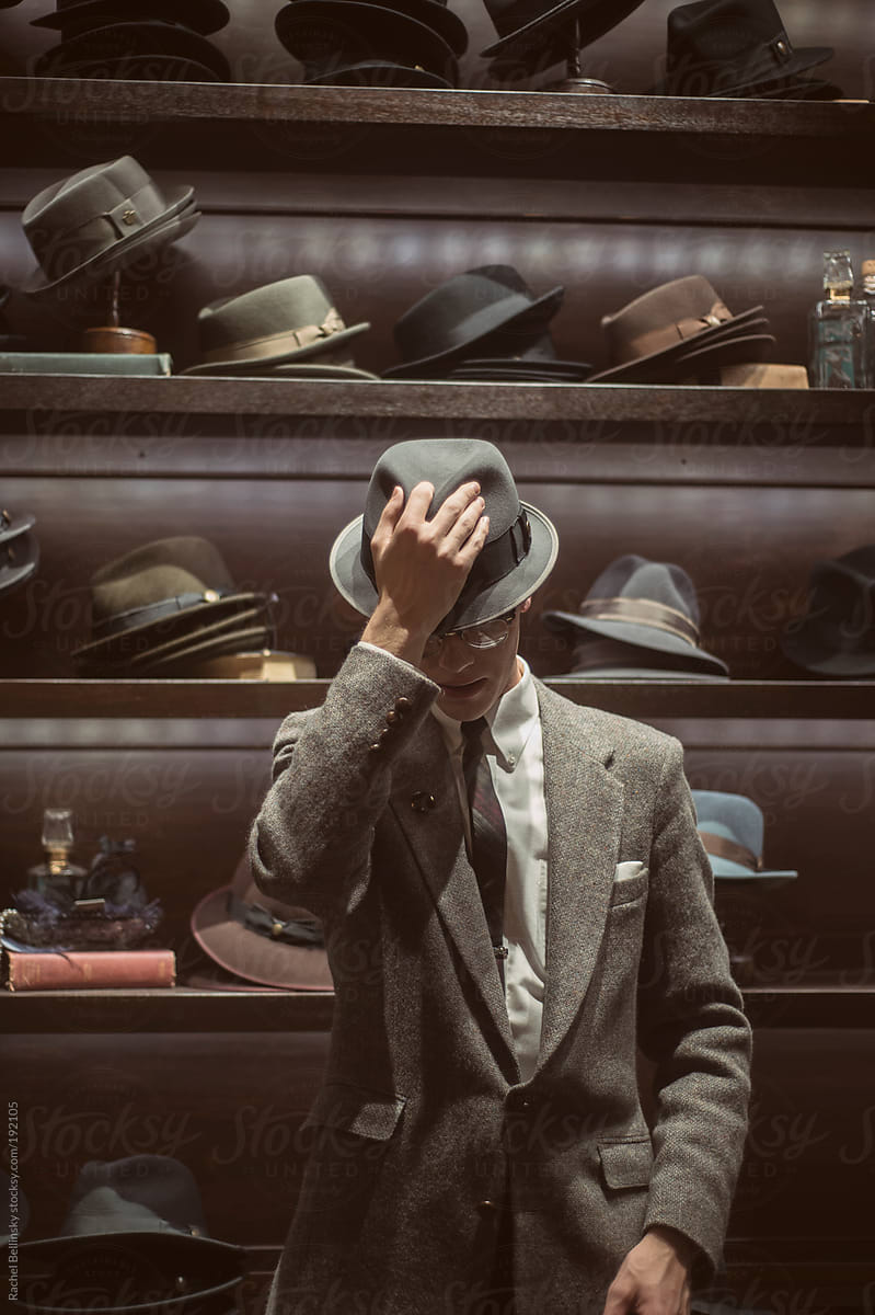 A dapper young man in a suit and tie tries on hats