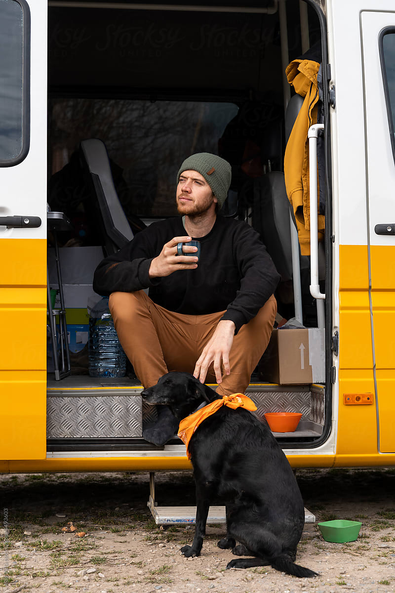 Portrait of happy man with coffee mug in camper van with dog