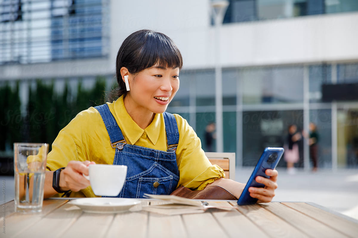 Smiling freelancer video calling on smart phone while enjoying coffee